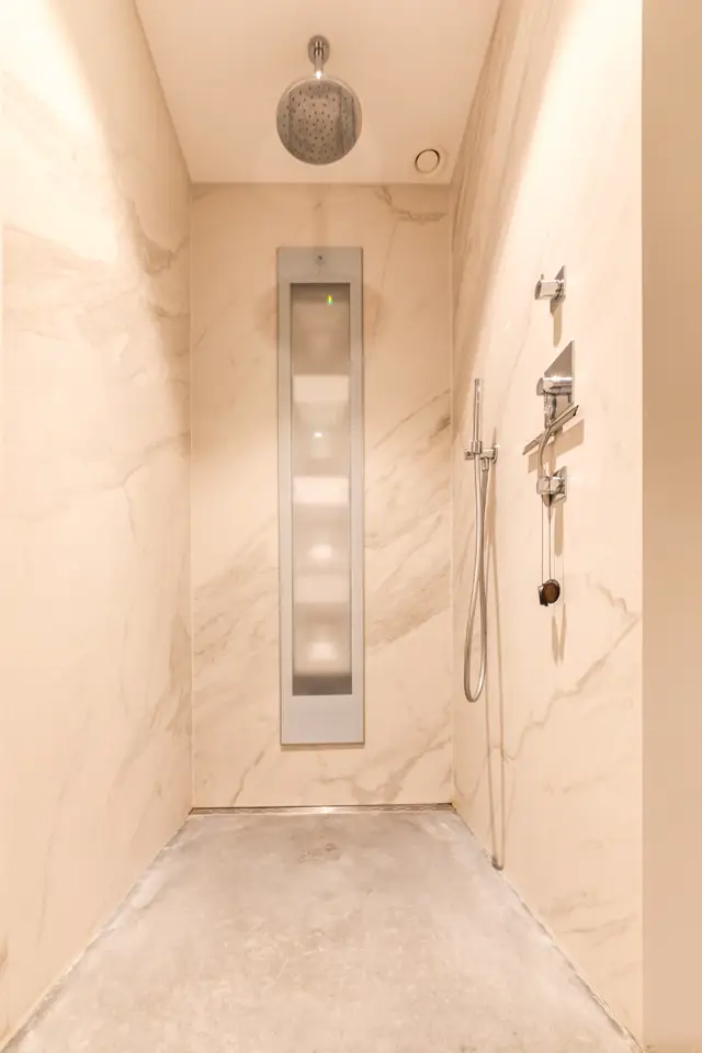 Een strakke, naadloze doucheruimte in warm beige met elegante chroom armaturen. De wanden zijn uniform afgewerkt met subtiele marmeringbij een zeer opgeruimde, geometrische indeling.