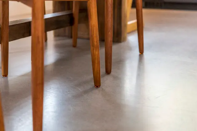 Minimalistisch interieur met elegante houten stoelen op een gladde, lichte naadloze vloer. De perfecte vlakheid en reflectie benadrukken de serene, opgeruimde uitstraling.