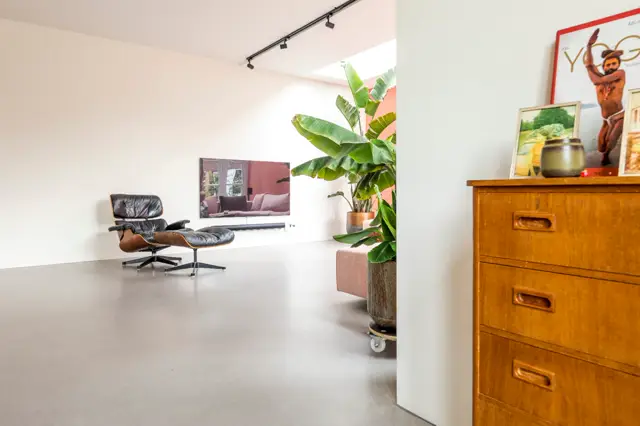 Minimalistische ruimte met een strakke naadloze vloer in warm grijs, waarin design en comfort samenkomen. Het licht stroomt natuurlijk binnen en benadrukt de schone lijnen en ruime opzet.