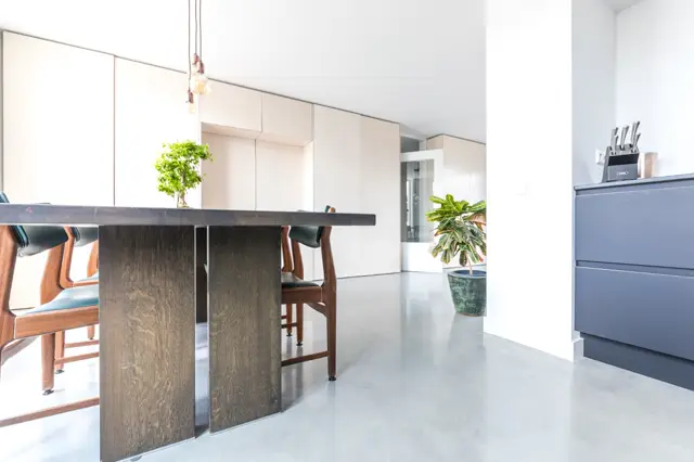 Een serene, lichte keukenruimte met naadloze vloer en wanden in warm wit en grijs. Natuurlijk licht, strakke lijnen, scandinavisch design met donker houten details en subtiele plantaccessoires.