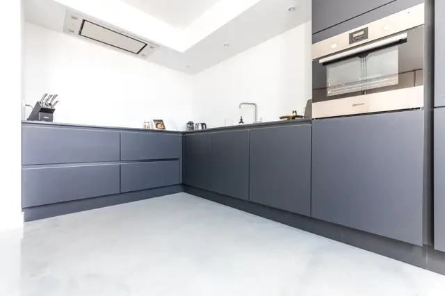 Strakke, minimalistisch ingerichte keuken met donkerblauwe kasten en lichte naadloze vloer. Het geheel straalt luxe en organisatie uit met schone lijnen en perfect afgestelde details.