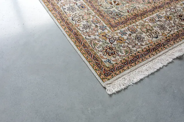 Een traditioneel oosters tapijt met rijke ornamenten ligt op een lichte, naadloze vloer. De vloer toont een subtiele textuur en neutrale kleurstelling die het tapijt perfect ondersteunt.
