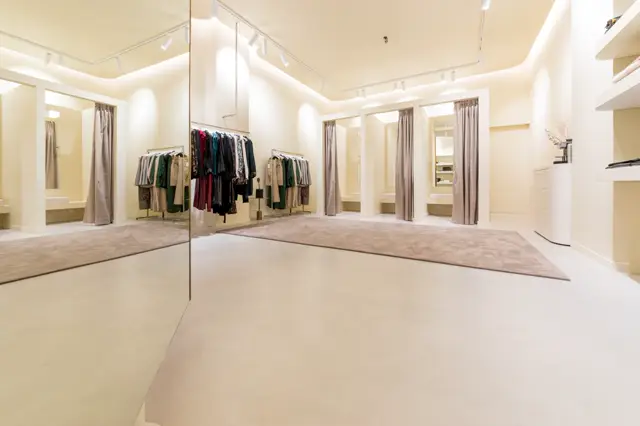 Strakke, lichte ankleedruimte met spiegelwanden en naadloze vloer in warm beige. Perfect uitgelichte ruimte met minimalistisch design en garderokes.