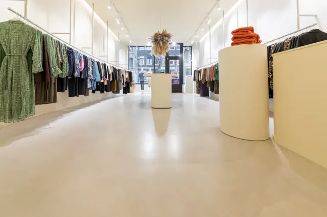 Ruimtelijk modeboutique met strakke witte wanden, blanke naadloze vloer en geometrische displayelementen. Het licht en opgeruimde interieur codeert luxe en exclusiviteit.