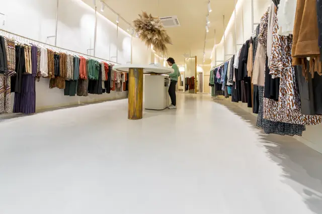 Strakke, lichte wintelruimte met een uitnodigende naadloze vloer in warm wit. De minimalistische inrichting met geleide verlichting en proper onderhouden wanden creëert een premiumgevoel.