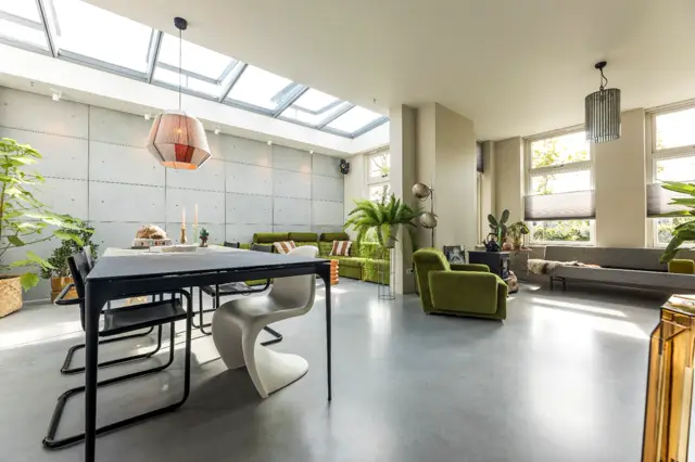 Ruime, licht woonkamer-eetkamer met grote raampartijen, glanzende naadloze vloer en minimalistisch design. Strakke wanden, duurzame meubels en veel groen creëren een serene, geordende sfeer.