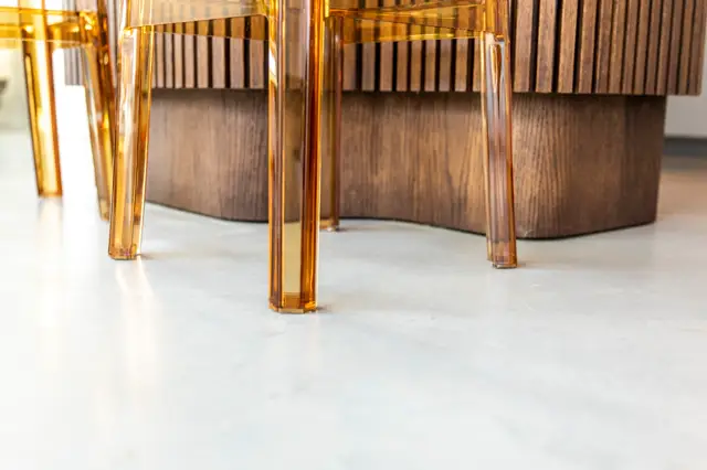 Moderne designstoelen met amberkleurige poten staan op een lichte, glanzende naadloze vloer. De compositie toont perfecte ruwheid en minimalistische elegantie met warm licht.