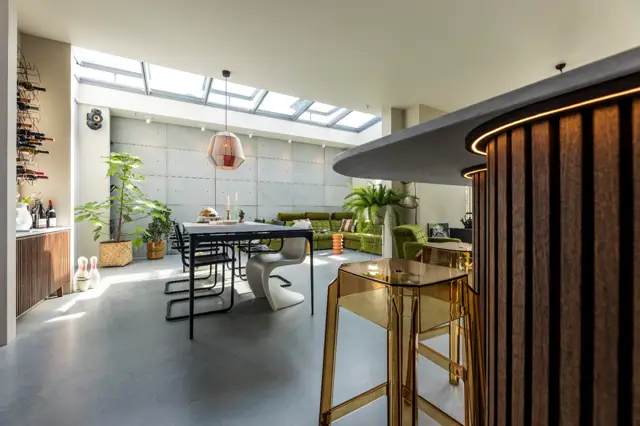 Ruime, lichte woonruimte met naadloze grijze vloer die het moderne interieur ondersteunt. Natuurlijk licht door grote ramen en skylight; strak design met groene accenten en elegante zwarte meubels.