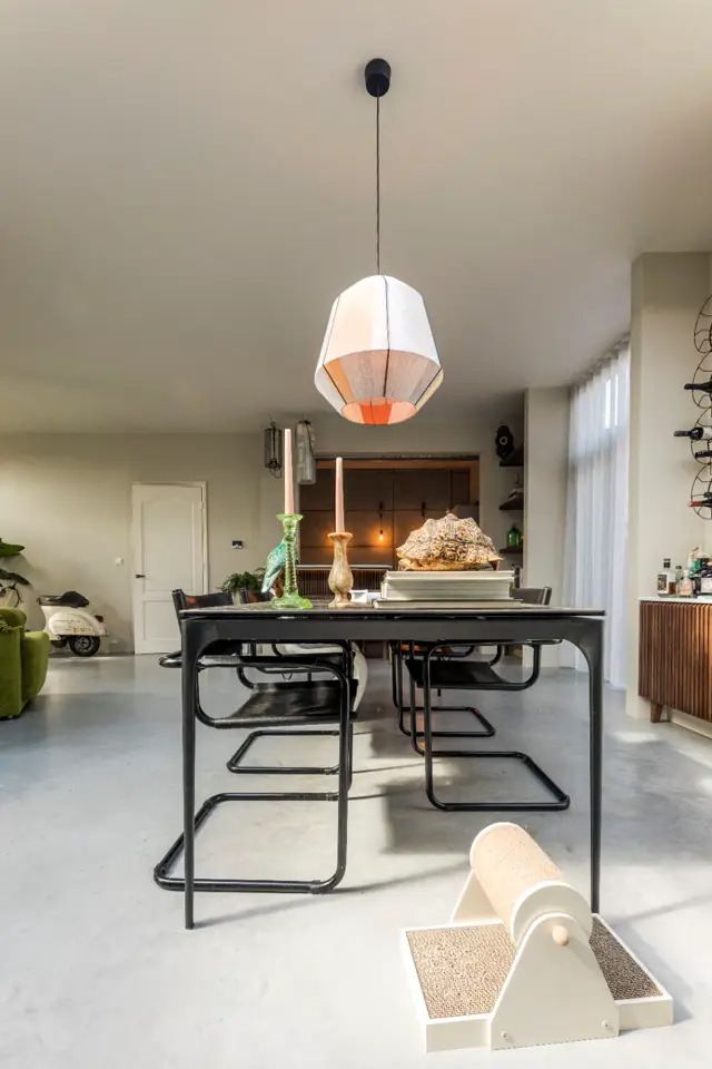 Spacieus interieur met een naadloze lichte vloer die naadloos aansluit op alle ruimten. Strakke lijnen, minimalistisch design met zwarte tafel, natuurlijk licht en rustige kleurpalette.