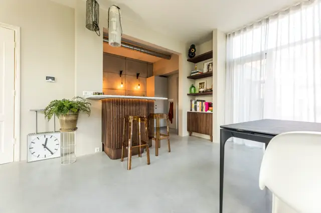 Ruimtelijk woon- en keukengebied met een lichte, continue naadloze vloer. Strakke lijnen, natuurlijk licht van grote ramen, warm houtaccenten en een opgeruimde, minimalistische inrichting.