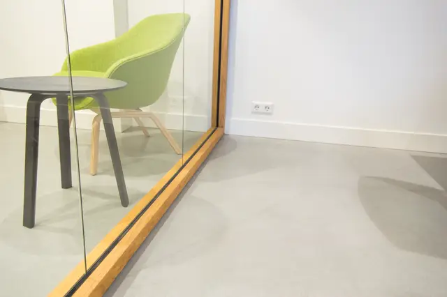 Een moderne kantoorruimte met een lichte naadloze vloer die naadloos aansluit op een glazen wand met houten frame. De ruimte straalt minimalistische elegantie uit met scherpe lijnen en perfecte afwerking.