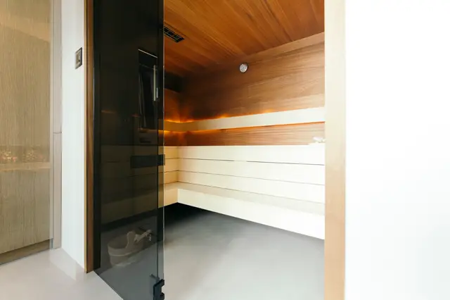 Een stijlvolle sauna met naadloze wanden in warm hout en crème, afgewerkt met een zwarte glazen deur. De ruimte straalt rust en verfijning uit met scherpe lijnen en perfecte afwerking.