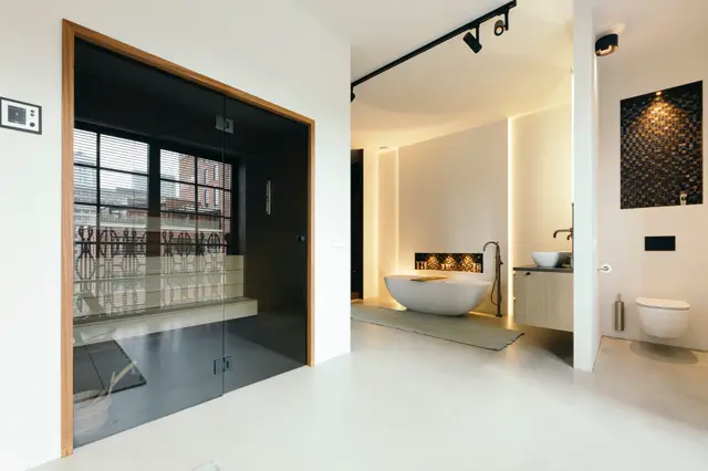 Serene badkamerruimte met strakke, naadloze vloer en wanden. Centraal een vrijstaand bad met ambient verlichting, douche achter glaswand, en minimalistisch design met natuurlijke houttinten en zwarte accenten.