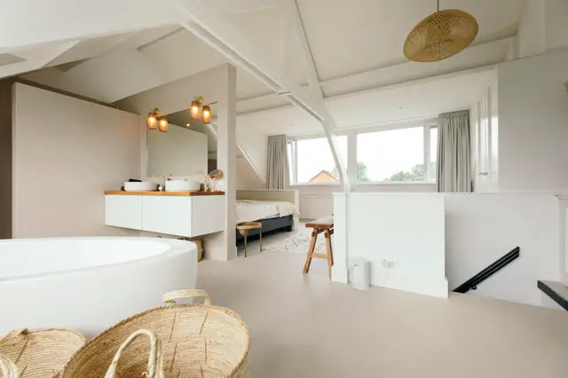 Ruime, licht ingestelde slaapkamer-badkamer combinatie met een puurwitte naadloze vloer. Subtiele hoekdetails, warm houtaccenten en natuurlijk licht creëren een serene, minimalistische esthetiek.