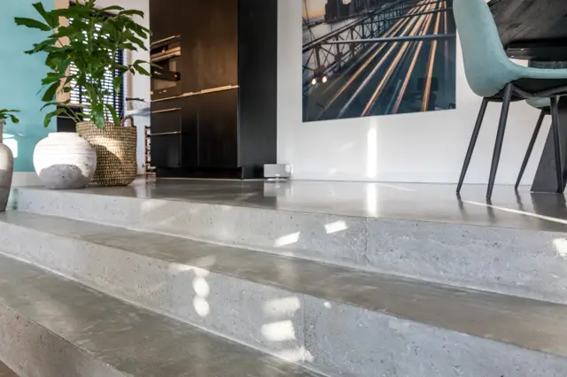 Strakke, lichte naadloze vloer in een modern open ruimte met natuurlijk licht, minimalistisch ingericht met groene plant en zwarte architectuurelementen.