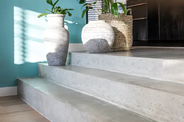 Een strakke trapopstelling met lichte naadloze wanden en traptreden, minimalistisch gestyleerd met witte plantenpotten en natuurlijke accessoires. Felle natuurlijke belichting met schaduwwerking creëert drama.