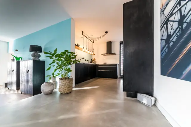 Licht, strak interieur met een uniforme naadloze vloer die vloeiend doorloopt van woonruimte naar keuken. Minimalistisch design met zwarte accenten, natuurlijk licht en groene planten.