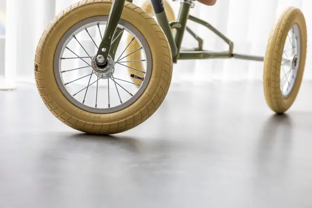 Close-up van een designwagen met gouden wielen op een lichte, naadloze vloer. De minimalistische styling en heldere belichting tonen de perfecte afwerking van de ondergrond.