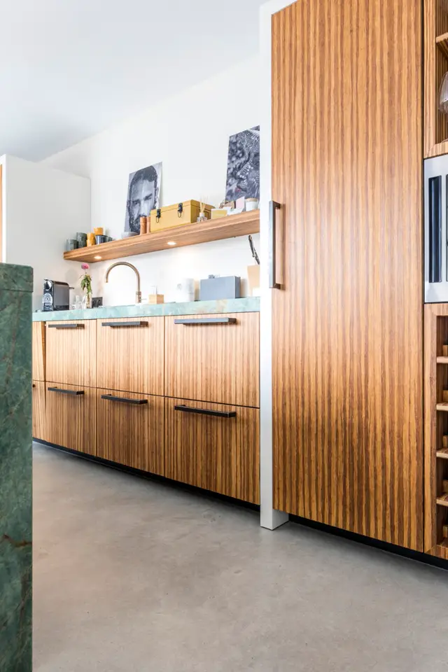 Moderne keukenruimte met witte wanden, houten frontale kastenwanden in warme tint, naadloze vloer in natuurlijke tinten en minimalistisch design. Rustige, opgeruimde styling met geïntegreerde verlichting.