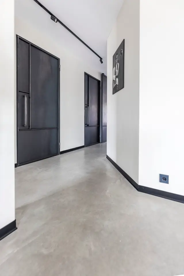 Strakke hal met witte wanden, zwarte deuren en een grijze naadloze vloer. Perfecte lijnen, schoon design en professionele belichting creëren een rustige, luxe sfeer.