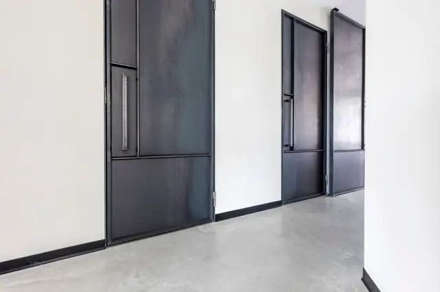 Strakke hal met naadloze lichte wand, glimmende zwarte deuren met glasdetails en subtiele metalen grepen. De naadloze vloer sluit perfect aan op de scherpe zwarte plint, creëerend een geraffigd, opgeruimd geheel.