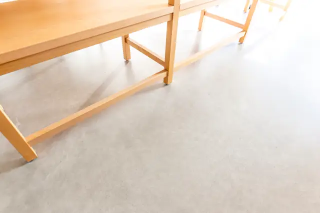 Minimalistisch interieur met een heldere, naadloze vloer in warme grijstint. Houten tafel en stoelen creëren een schoon, opgeruimd beeld met perfecte scheepslijnen.