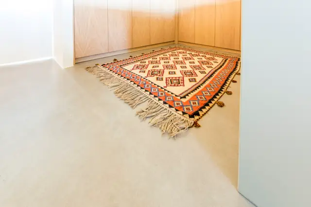 Minimalistisch interieur met een zeer lichte, uniforme naadloze vloer. Een geométrisch tapijt in warme aardetinten biedt contrast en textuur in de verder strakke ruimte.