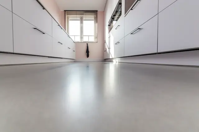 Strakke, lichte keuken met witte kasten en een glanzende naadloze vloer. Overvloedig natuurlijk licht van bovenaf creëert een schoon, opgeruimd interieur met perfecte geometrische lijnen.