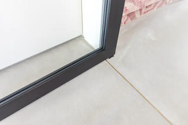 Gedetailleerde close-up van een lichte naadloze vloer die elegant aansluit op een moderne zwarte deurframe. De overgang toont perfecte afwerking en minimalistisch design.