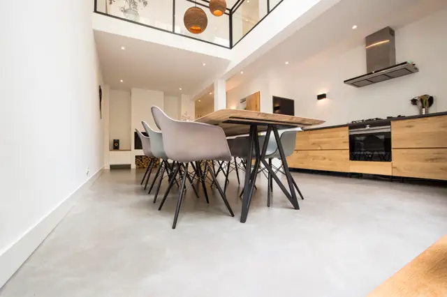 Strakke, lichte open ruimte met naadloze vloer, minimalistisch interieur in wit en houtaccenten. Moderne keuken, eethoek met designstoelen en natuurlijk licht van bovenaf.