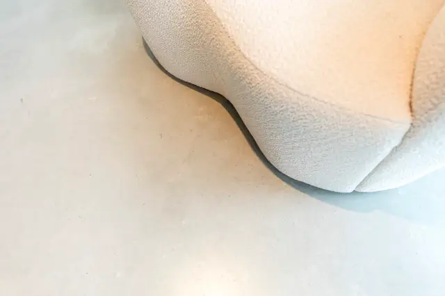 Close-up detail van een lichte naadloze wand met subtiele textuur en organische, vloeiende lijnen. De zachte schaduwwerking benadrukt de verfijnde afwerking en minimalistische esthetiek.