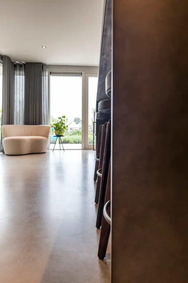 Ruim, licht interieur met glanzende naadloze vloer in warme tint. Minimalistische inrichting met beige fauteuil, grote ramen met uitzicht en strakke afwerking.