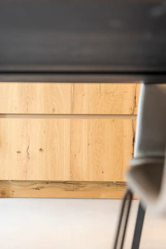 Detail van een moderne wand met warme houten panelen en een naadloze vloer in wit, met subtiele schaduwlijnen die het vakmanschap benadrukken.