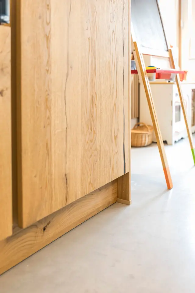 Detailshot van een lichte naadloze vloer die elegant aansluit op een warme houten wandelement. De scherpe overgang en minimalistische afwerking tonen vakmanschap.