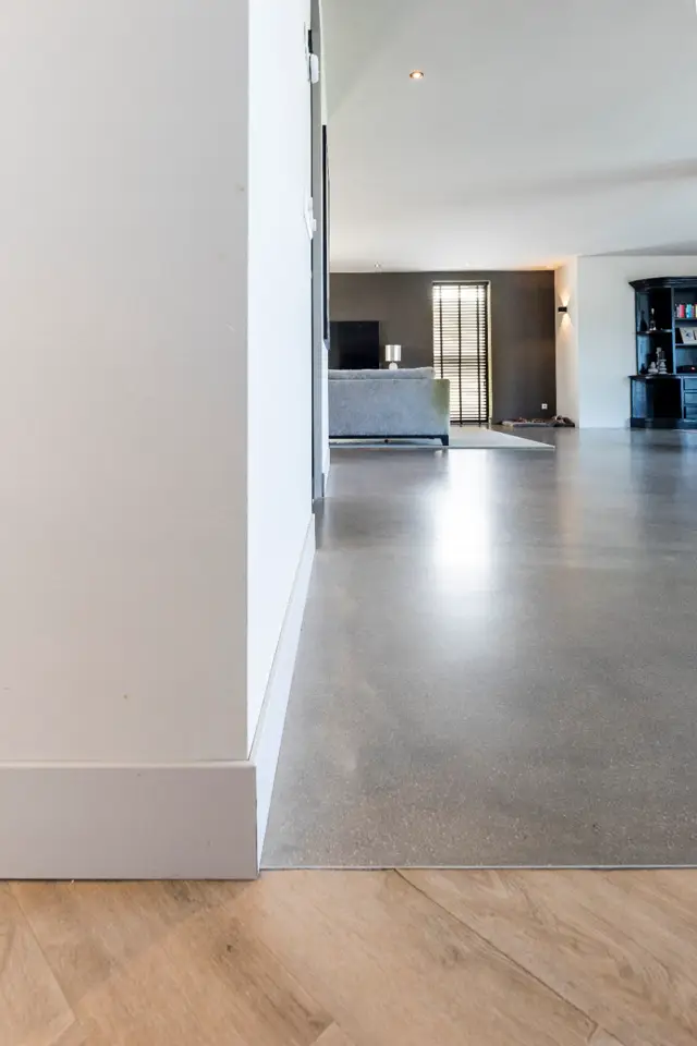 Ruime, licht ingevallen hal met naadloze vloer die elegant overloopt naar de woonkamer. Het materiaal reflecteert subtiel het natuurlicht en creëert een minimalistisch, schoon geheel.