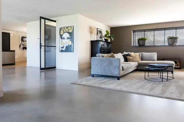 Luxe penthouse met glanzende naadloze vloer die zich uitstrekt over de gehele open woon- en keukenzone. Strakke witte wanden, minimalistische inrichting en perfect verzorgde detailafwerking.