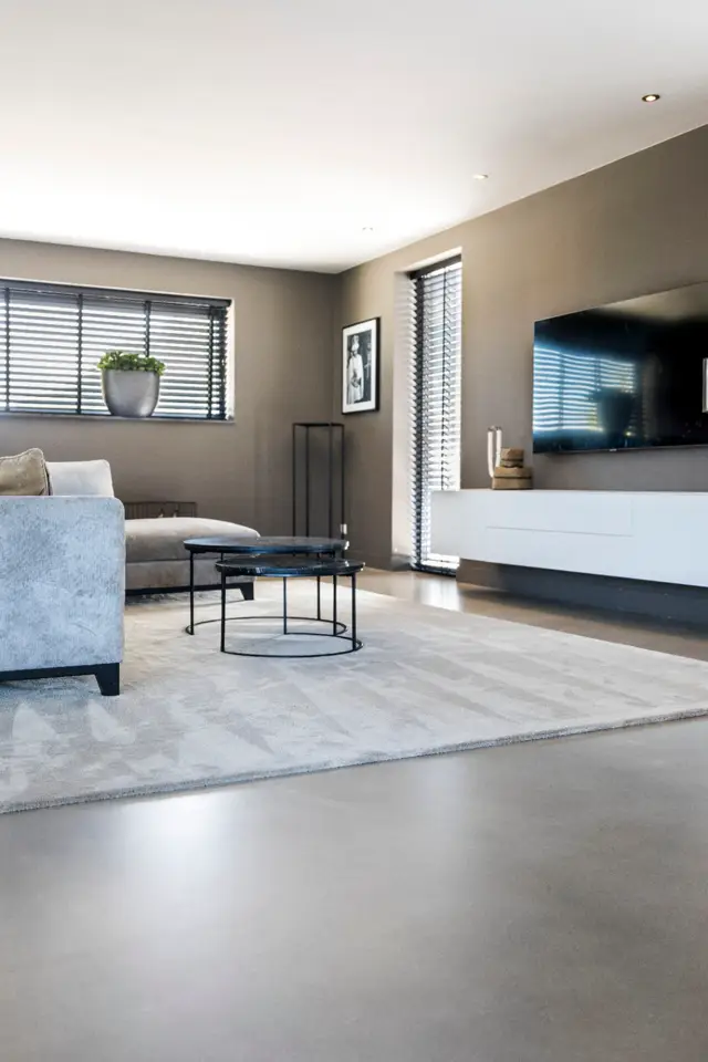 Luxueuze woonkamer met een grijze naadloze vloer die naadloos overloopt in een uitgekiend interieur. Strakke lijnen, zachte belichting en minimalistisch meubilair creëren een rustgevend geheel.