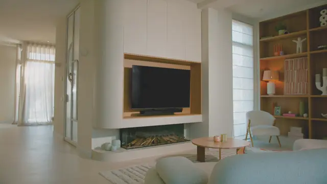 Serene, lichte woonkamer met een volledig naadloze vloer in warm crème. Het interieur toont een strak ingebouwde haard met TV, houtaccenten, opgeruimde open kasten en minimalistisch meubilair met natuurlijke materialen.