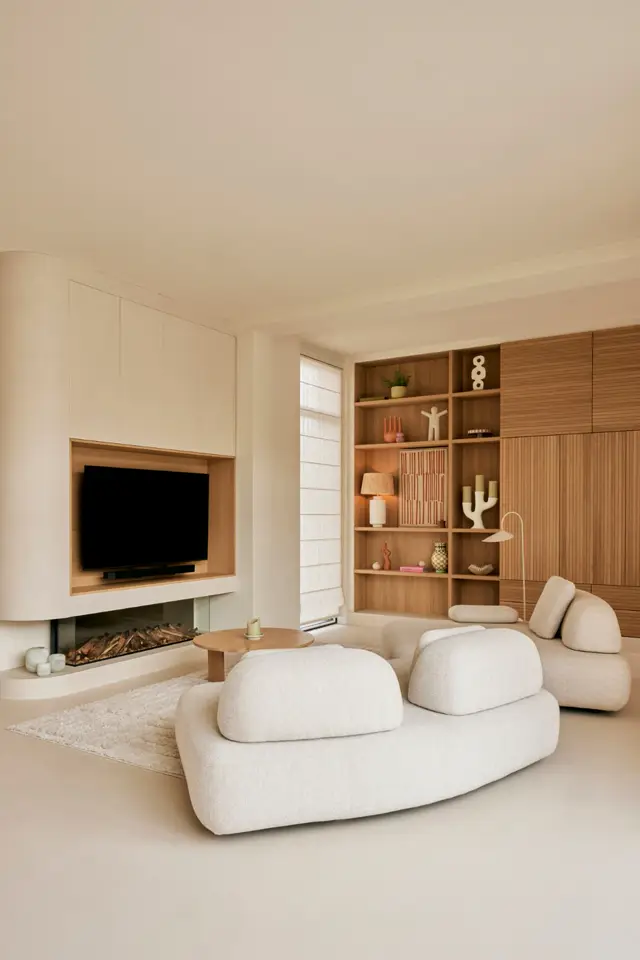 Lichte, strak ingerichte woonkamer met harmonische beige tonen. Een naadloze vloer in warm zandkleur loopt ononderbroken door de ruimte, ondersteund door ingebouwde houten elementen en designer meubels.
