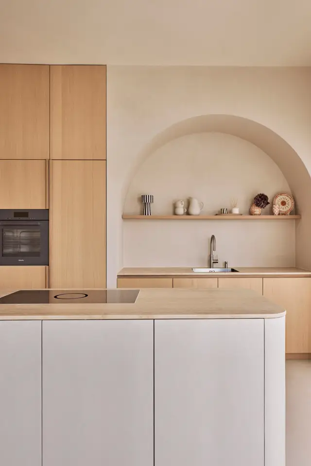Een serene keukenruimte met natuurlijke houttinten, een elegante boogvormige niswan en naadloze wand. Het interieur ademt rust uit met schone lijnen, curated styling en precieze detaillering.