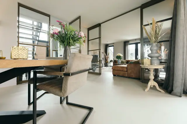 Ruime, moderne woonkamer met een continue, lichte naadloze vloer die een serene uitstraling creëert. De ruimte ademt luxe door schone lijnen, spiegelwanden en zorgvuldig gestyled interieur.