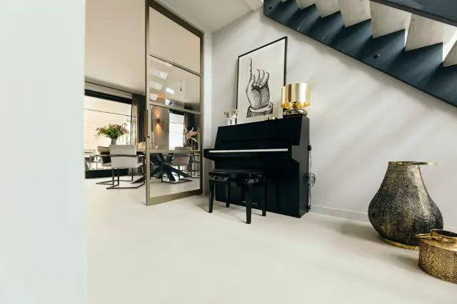 Stijlvolle open hal met glanzende witte naadloze vloer, zwarte trap met houten treden, en elegant ingericht met zwarte piano, gouden accessoires en minimalistisch design.