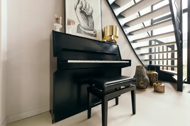 Stijlvolle hal met minimalistische naadloze vloer in warm grijs, fraai ingericht met een zwarte vleugelpiano, moderne trap met open treden en luxe design-accessoires.