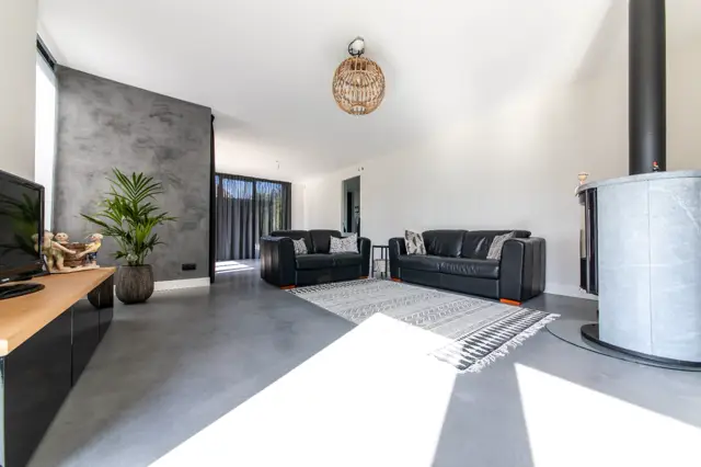 Ruime, licht ingerichte woonkamer met naadloze vloer in grijs. Minimalistisch ingericht met zwarte lederen banken, veel daglicht en subtiele natuurlijke accenten.