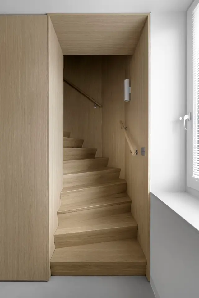 Een strakke, lichte trappenhal met naadloze houtafwerking op wanden en treden. Het ontwerp straalt rust en ordening uit door schone lijnen, perfecte afwerking en hoogwaardige materiaaldetails.