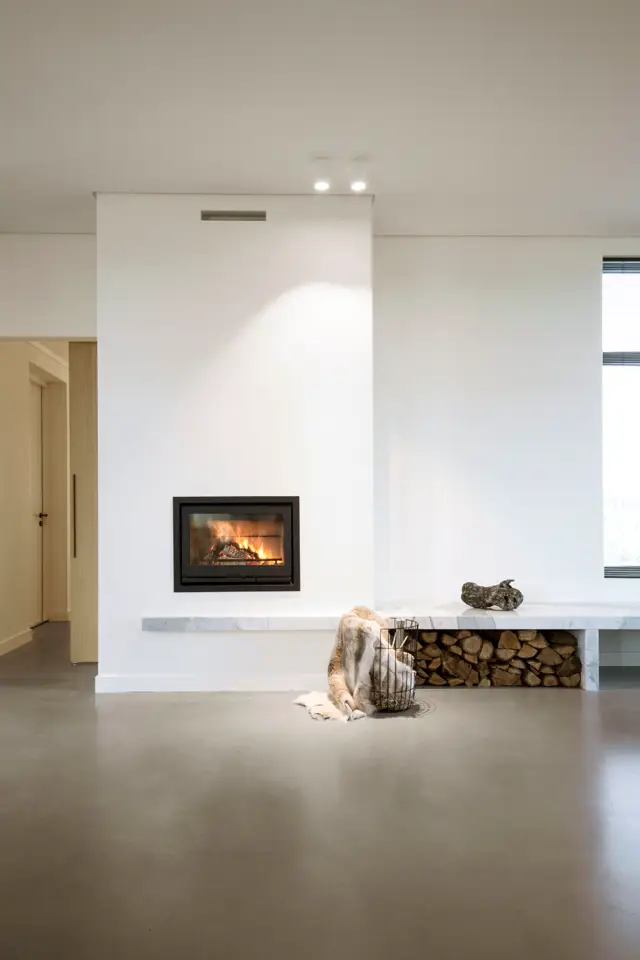 Een strak ontwerp met een ingebouwde haard in een zuiver wit accent, ondersteund door een naadloze vloer in grijs. Opgeruimde, open ruimte met perfect symmetrie en subtiele styling.