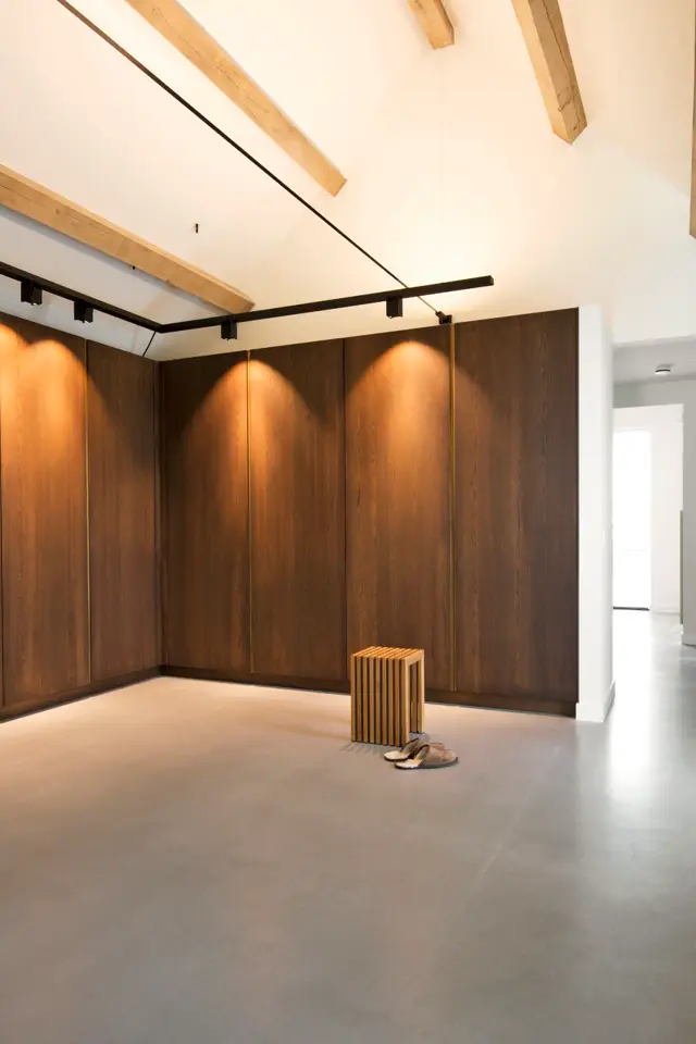 Een strakke, lichte ruimte met donkerhouten wandpanelen en subtiele spotverlichting. De naadloze vloer en schone architectuur creëren een serene, galerieachtige sfeer.