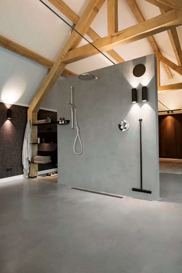 Strakke badkamer met grijs naadloze wand, minimalistisch design en ingebouwde douche. Natuurlijke houten spanten geven warmte aan het lichte, ruime interieur.