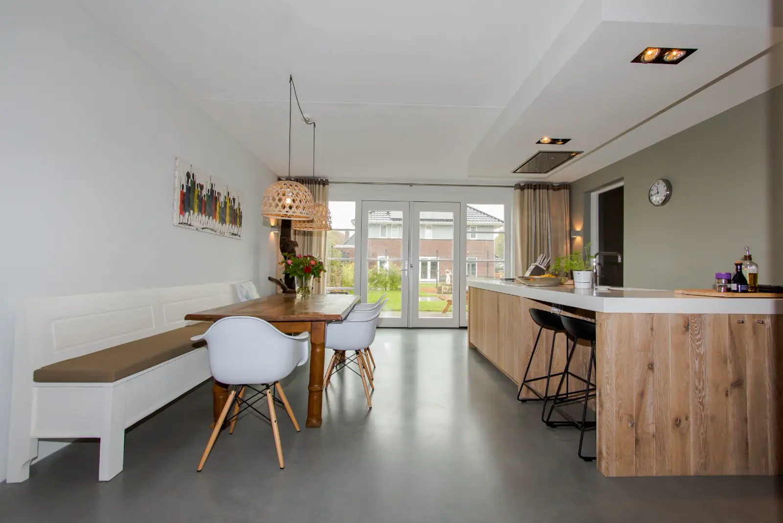 Ruime, lichte keuken-eetkamer met grijze naadloze vloer die naadloos aansluit op het woongedeelte. Strakke witte wanden, houten accenten en doordachte inrichting creëren een minimalistisch luxe geheel.