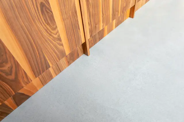 Strakke compositie van warme houten panelen die contrasteren met een lichte, uniforme naadloze vloer. Scherpe lijnen en perfecte afwerking creëren een minimalistisch, luxe effect.